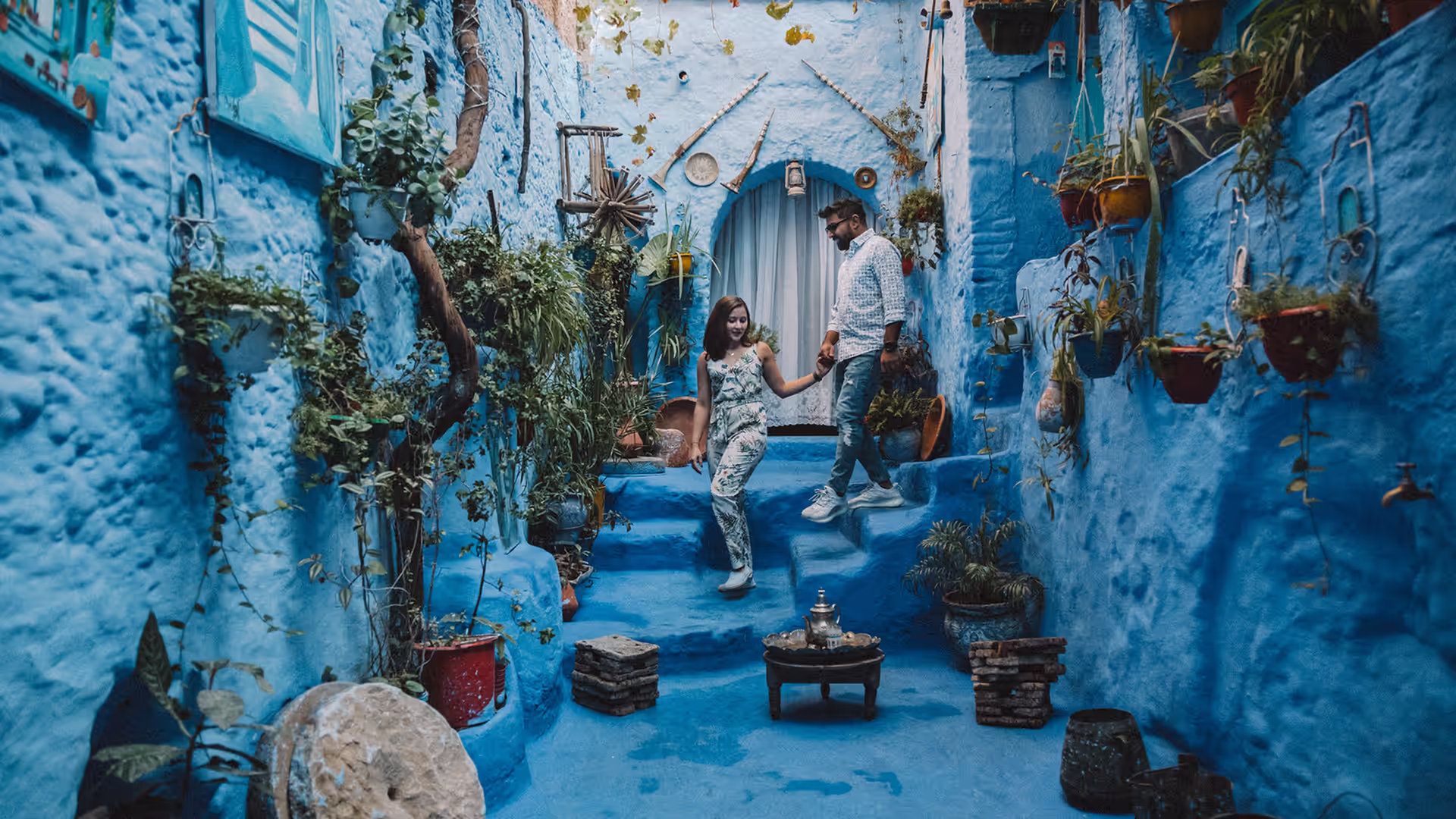 Couple standing hand in hand in a plant-filled blue lane in Chefchaouen