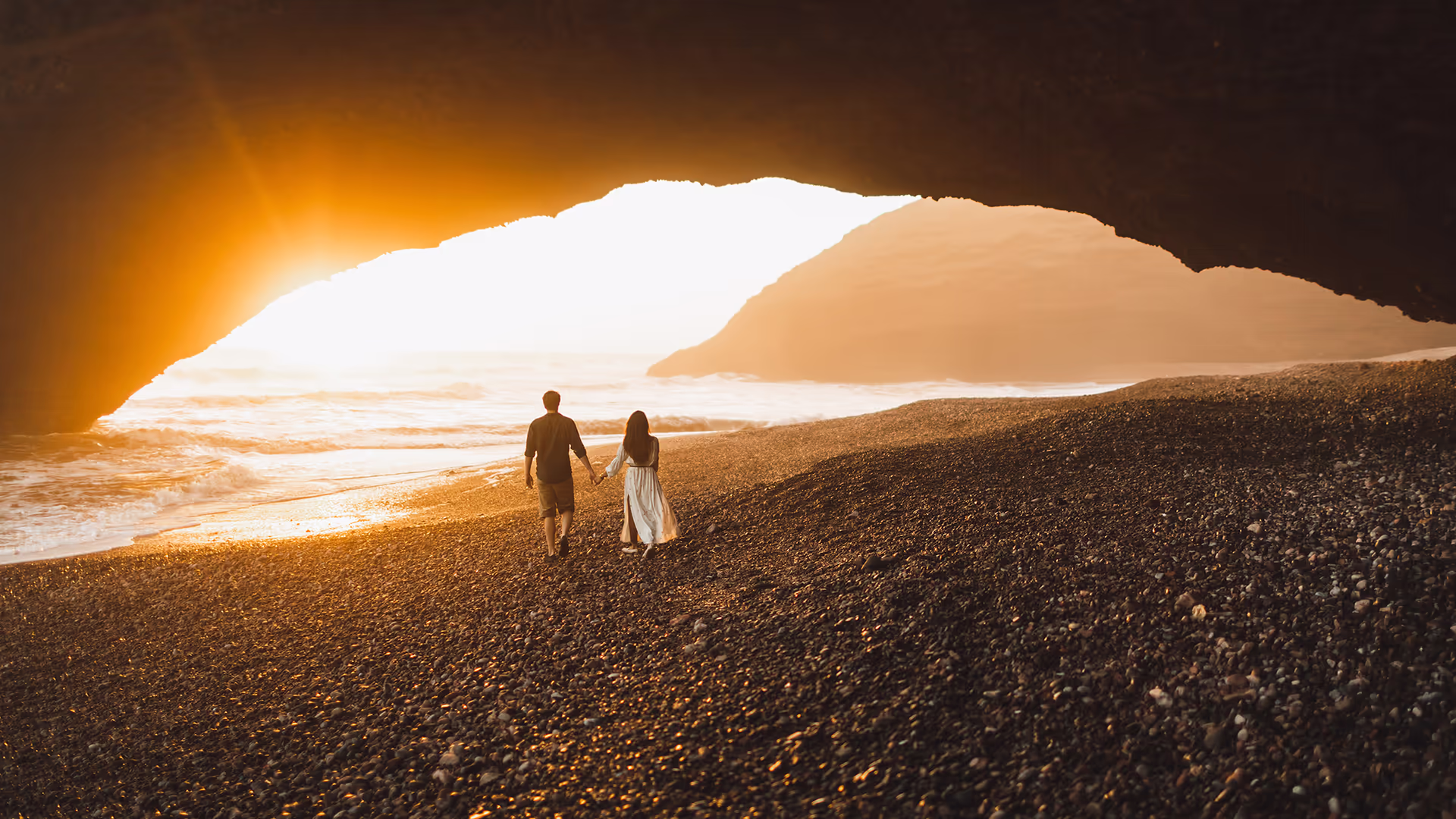 Couple walking on wet sand beneath the great rock arch at Legzira beach