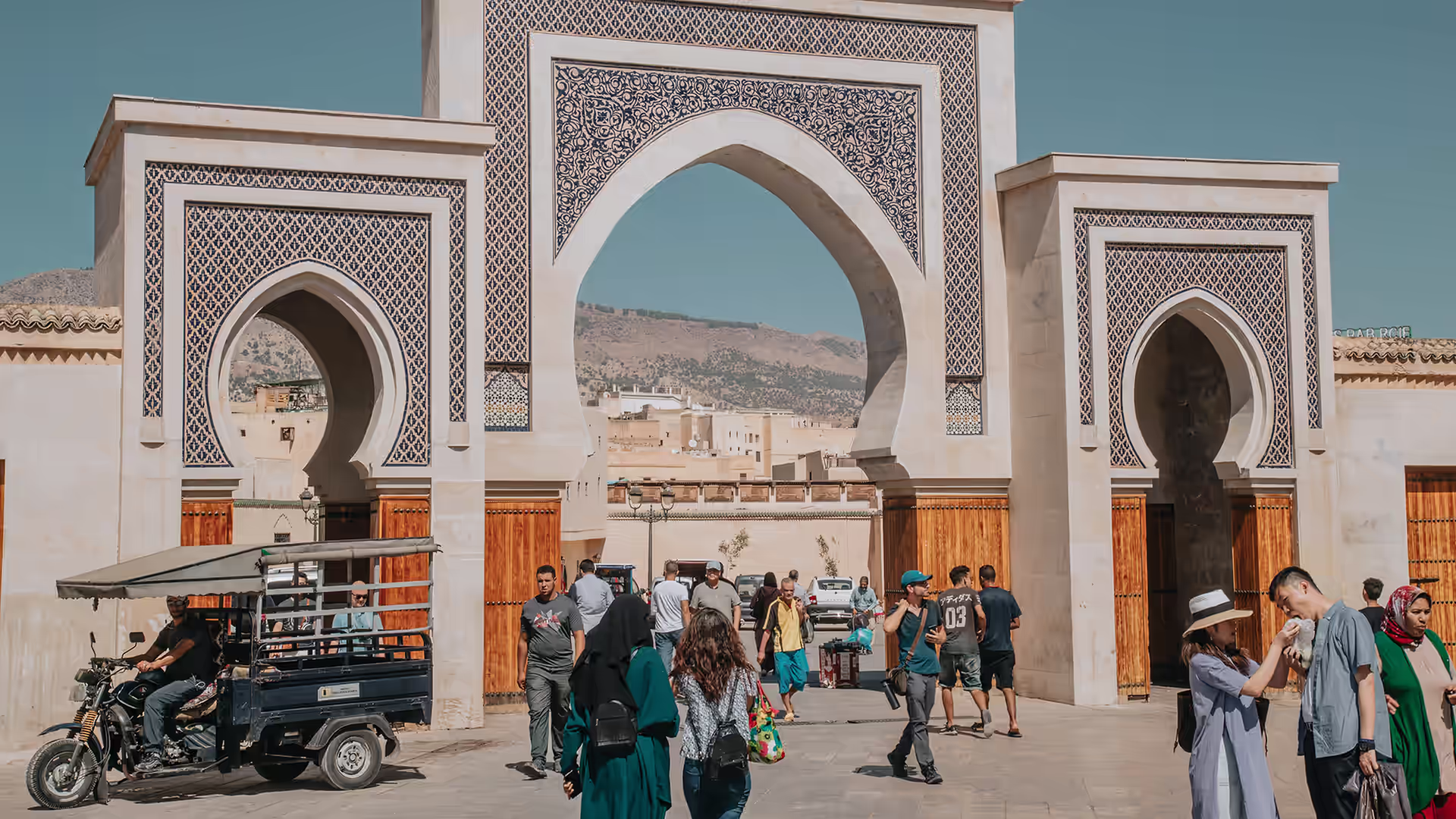 Triple-arched tiled gate into the Fez medina with people passing through